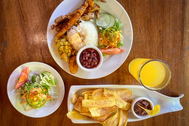 Assorted meal with rice, beans, meat, salad, plantains, and juice on a wooden table.