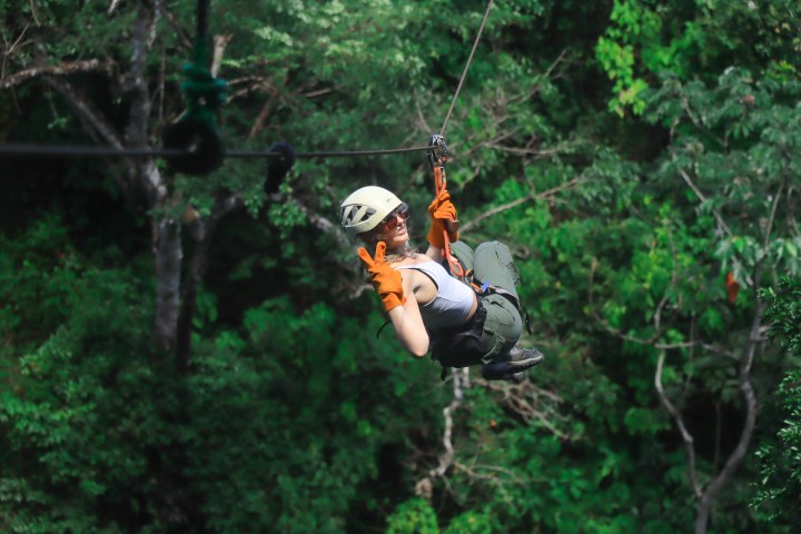Person ziplining through a dense forest, wearing a helmet and gloves.