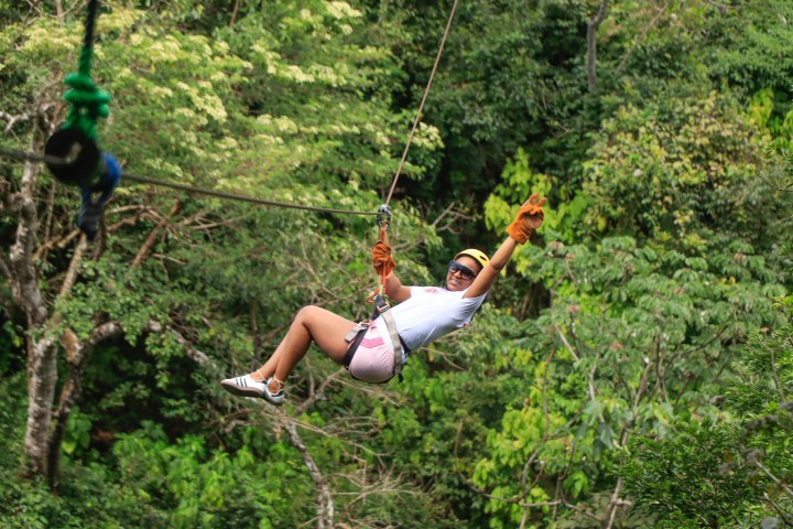 Person wearing helmet and gloves ziplining through a forested area.