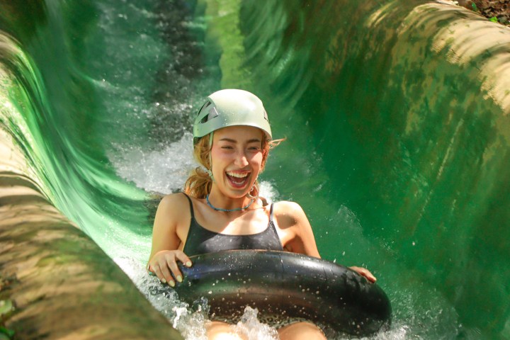 Smiling woman in helmet tubing down a green water slide.