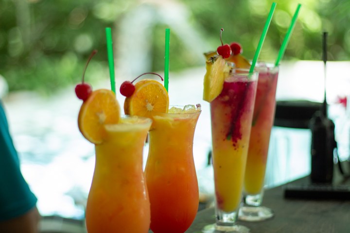 Colorful cocktails with fruit garnishes and straws on a table with blurred background.