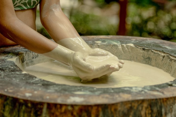 Person's hands mixing liquid in a wooden bowl outdoors.
