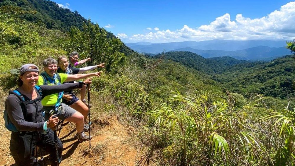 Four hikers pointing at a scenic mountain view under a bright blue sky.