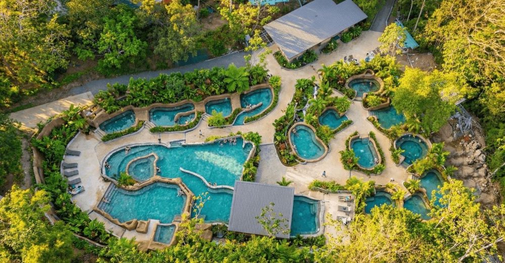 Aerial view of a tropical resort with multiple swimming pools surrounded by lush greenery.