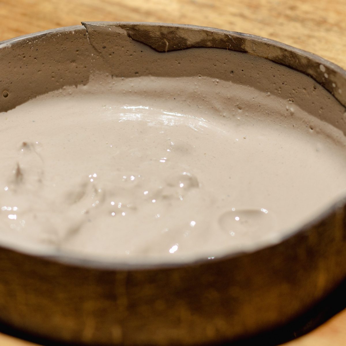Wet clay in a round metal mold on a wooden surface.
